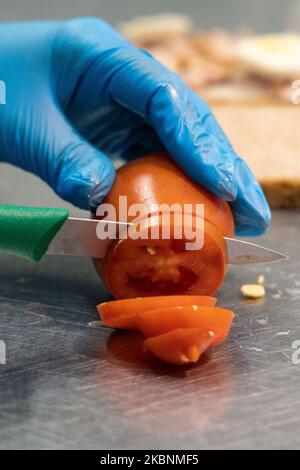 Comptoir déli frais dans un hypermarché de Cora. Employé préparant un sandwich avec du pain coupé en tranches. Ici, couper une tomate Banque D'Images