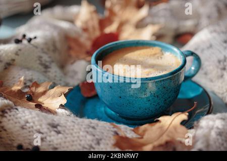 Écharpe tricotée blanche, tasse de café bleue et feuilles jaunes sèches Banque D'Images