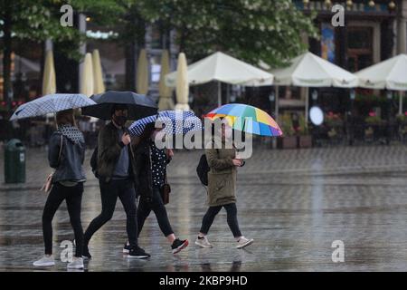 Les personnes portant un masque de protection marchent sur la place principale du marché de Cracovie par temps pluvieux. La pluie est revenue dans la région de Cracovie et des conditions météorologiques variables avec des températures entre 15 et 20 degrés C sont prévues pour les 10 prochains jours. Lundi, 25 mai 2020, à Cracovie, en Pologne. (Photo par Artur Widak/NurPhoto) Banque D'Images