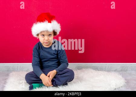 drôle de garçon avec l'expression sérieuse assis avec chapeau de noël Banque D'Images