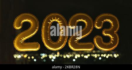 Ballons de papier d'aluminium gonflable d'or numéros 2023 sur la fenêtre contre le fond de la ville de nuit, dans la lumière de néon. Nouvel an 2023, noël. Célébration de Noël et du nouvel an 2023. Banque D'Images