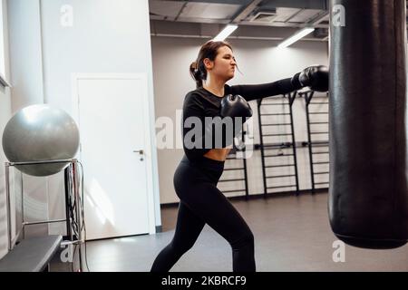 Une femme de boxe latine forte saute de coup de pied à un énorme sac de poinçonnage à la salle de fitness. Entraînement de fille athlétique Muay Thai boxe pour le culturisme et la vie saine Banque D'Images