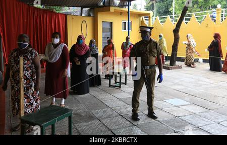 Les électeurs sri-lankais qui portent un masque facial se tiennent en ligne pour voter alors qu'un policier se tient à la garde lors d'une élection simulée avant les élections législatives à Colombo, au Sri Lanka, sur 20 juin 2020. (Photo de Thharaka Basnayaka/NurPhoto) Banque D'Images
