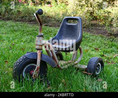 Tricycle vieux et rouillé pour enfants sur une pelouse verte Banque D'Images