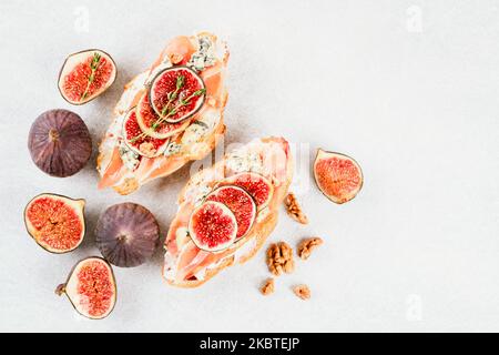 Vue ci-dessus sur un croissant frais de bruschetta avec figues mûres, fromage bleu, prosciutto, noix et herbes sur fond de table en béton blanc avec copie de spac Banque D'Images