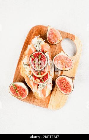 Image verticale - croissant frais bruschetta avec figue mûre, fromage bleu, prosciutto, noix et herbes sur planche à découper en bois sur tabl en béton blanc Banque D'Images