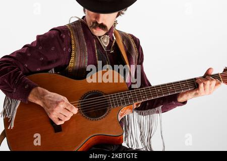 Portrait d'un homme avec moustaches dans des vêtements de style campagnard jouant de la guitare isolée sur fond blanc. Choix des accords Banque D'Images