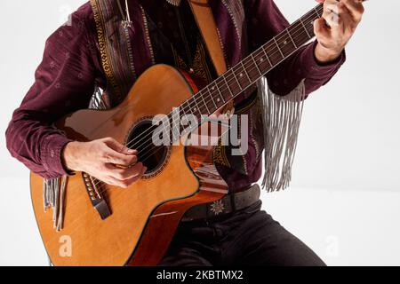 Image rognée de l'homme dans des vêtements de style cow-boy vintage jouant de la guitare, en choisissant des accords isolés sur fond blanc Banque D'Images