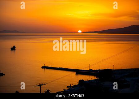 Coucher de soleil de rêve sur la ville de Mykonos et le petit port pendant l'heure d'or avant le crépuscule avec le ciel changeant de couleurs rouge, orange et chaudes tandis que le soleil descend derrière la mer Égée au-dessus de la ville de Mykonos ou Chora, à l'île de Myconos dans les Cyclades, mer Egée en Grèce. La célèbre île grecque méditerranéenne est surnommée l'île des vents avec des bâtiments traditionnels blanchis à la chaux comme des moulins à vent ou une petite église. Mykonos est une île populaire pour les célébrités et les touristes qui veulent faire la fête dans la vie nocturne animée, l'île est également considérée gay friendly. Le gouvernement grec a relancé l'été Banque D'Images