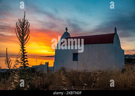 Coucher de soleil de rêve pendant l'heure d'or avec une petite chapelle traditionnelle juste avant le crépuscule avec le ciel changeant de couleurs rouge, orange et chaudes tandis que le soleil descend derrière la mer Égée au-dessus de la ville de Mykonos ou de Chora, à l'île de Myconos dans les Cyclades, la mer Égée en Grèce. La célèbre île grecque méditerranéenne est surnommée l'île des vents avec des bâtiments traditionnels blanchis à la chaux comme des moulins à vent ou une petite église. Mykonos est une île populaire pour les célébrités et les touristes qui veulent faire la fête dans la vie nocturne animée, l'île est également considérée gay friendly. Le gouvernement grec a relancé le touriste d'été Banque D'Images