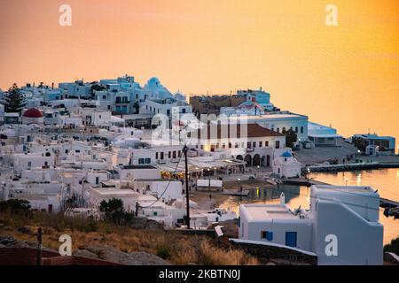 Coucher de soleil de rêve sur la ville de Mykonos et le petit port pendant l'heure d'or avant le crépuscule avec le ciel changeant de couleurs rouge, orange et chaudes tandis que le soleil descend derrière la mer Égée au-dessus de la ville de Mykonos ou Chora, à l'île de Myconos dans les Cyclades, mer Egée en Grèce. La célèbre île grecque méditerranéenne est surnommée l'île des vents avec des bâtiments traditionnels blanchis à la chaux comme des moulins à vent ou une petite église. Mykonos est une île populaire pour les célébrités et les touristes qui veulent faire la fête dans la vie nocturne animée, l'île est également considérée gay friendly. Le gouvernement grec a relancé l'été Banque D'Images