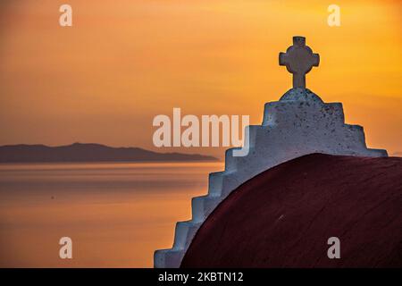 Coucher de soleil de rêve pendant l'heure d'or avec une petite chapelle traditionnelle juste avant le crépuscule avec le ciel changeant de couleurs rouge, orange et chaudes tandis que le soleil descend derrière la mer Égée au-dessus de la ville de Mykonos ou de Chora, à l'île de Myconos dans les Cyclades, la mer Égée en Grèce. La célèbre île grecque méditerranéenne est surnommée l'île des vents avec des bâtiments traditionnels blanchis à la chaux comme des moulins à vent ou une petite église. Mykonos est une île populaire pour les célébrités et les touristes qui veulent faire la fête dans la vie nocturne animée, l'île est également considérée gay friendly. Le gouvernement grec a relancé le touriste d'été Banque D'Images