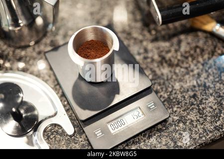 Le café fraîchement moulu est pesé avec précision sur une balance de cuisine dans un récipient en aluminium. Banque D'Images