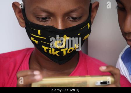 Un garçon portant un masque avec le logo TikTok utilise un téléphone portable à l'extérieur des volets d'une boutique à Mumbai, Inde sur 29 juillet 2020. (Photo par Himanshu Bhatt/NurPhoto) Banque D'Images