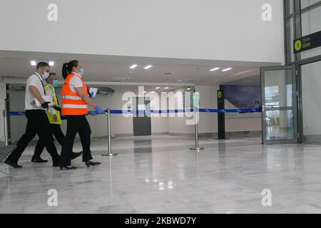 Le personnel de l'aéroport et de la compagnie aérienne marche avec des masques à l'intérieur de la zone des portes du terminal. Vol au départ de l'aéroport international de Mykonos JMK LGMK en Grèce. Passagers avec masques faciaux et mesures de protection comme gants, désinfectant pour les mains, sièges de blocage, signes sociaux de distancement, etc., vus aux comptoirs d'enregistrement, au terminal principal de départ, aux portes et en marchant vers l'avion, un avion turbopropulseur Olympic Air Bombardier DHC-8-400 avec enregistrement SX-OBA. L'aéroport appartient au gouvernement grec mais est exploité par Fraport Grèce depuis le 11 avril 2017 après les efforts de privatisation de 2015. O Banque D'Images