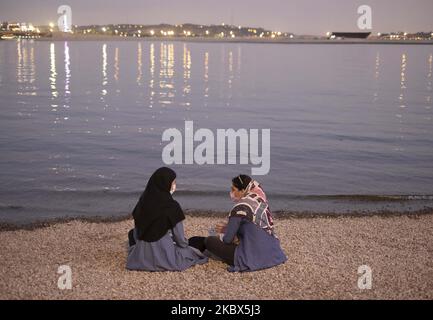 Deux femmes iraniennes portant un masque facial protecteur se parlent l'une avec l'autre alors qu'elles s'assoient sur la rive du lac Chitgar, dans le complexe récréatif Chitgar, dans le nord-ouest de Téhéran, au coucher du soleil, à la suite de l'épidémie de COVID-19 en Iran, au 13 août 2020. Les gens qui vivent à Téhéran semblent s'habituer au nouveau coronavirus et utiliser le masque comme une routine quotidienne. (Photo de Morteza Nikoubazl/NurPhoto) Banque D'Images