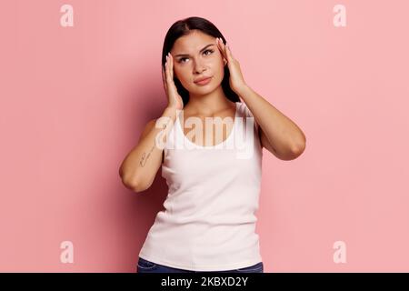 Femme ayant mal de tête. Isolé sur fond rose. Elle se tient debout avec douleur isolée sur fond de studio branché. Portrait de femme mi-longueur. Humain Banque D'Images