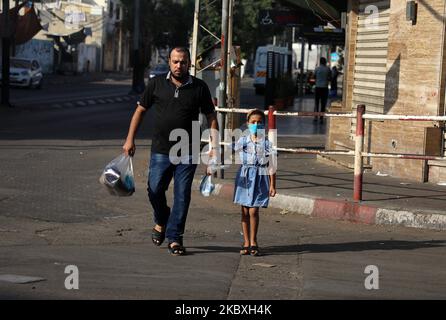 Une fille palestinienne portant un masque facial protecteur marche avec son père lors d'un confinement après que Gaza ait signalé ses premiers cas de COVID-19 dans la population générale, dans la ville de Gaza, à 25 août 2020. (Photo de Majdi Fathi/NurPhoto) Banque D'Images