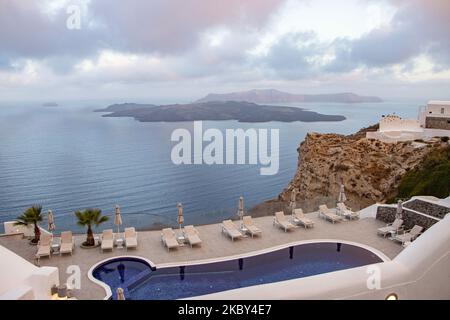 Piscine dans un hôtel 5 étoiles avec chaises longues et serviette donnant sur une belle vue sur la Caldera sur la mer Égée avec architecture traditionnelle méditerranéenne blanchie à la chaux des maisons et des stations. L'île de Santorini dans les Cyclades, Grèce pendant une chaude journée ensoleillée d'été. Santorini est généralement surpeuplé car il est célèbre pour son coucher de soleil attirant principalement des couples du monde entier pour la vue magique du coucher de soleil sur le volcan, Mais cette année, en raison de la pandémie du coronavirus Covid-19, il y a moins d'arrivées que d'habitude, ce qui réduit également le revenu du PIB du compte Banque D'Images