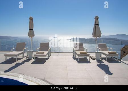 Piscine dans un hôtel 5 étoiles avec chaises longues et serviette donnant sur une belle vue sur la Caldera sur la mer Égée avec architecture traditionnelle méditerranéenne blanchie à la chaux des maisons et des stations. L'île de Santorini dans les Cyclades, Grèce pendant une chaude journée ensoleillée d'été. Santorini est généralement surpeuplé car il est célèbre pour son coucher de soleil attirant principalement des couples du monde entier pour la vue magique du coucher de soleil sur le volcan, Mais cette année, en raison de la pandémie du coronavirus Covid-19, il y a moins d'arrivées que d'habitude, ce qui réduit également le revenu du PIB du compte Banque D'Images