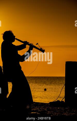 Une photo verticale d'un musicien silhoueté jouant sur la mer à l'aube Banque D'Images