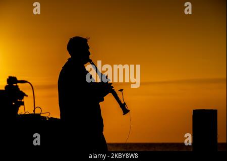 Un musicien silhoueté jouant sur la mer contre un ciel de lever du soleil Banque D'Images