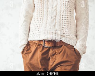 Femme en pull blanc à maille torsadée avec motif scandinave et pantalon chino marron avec ceinture en cuir. Vêtements décontractés pour un temps de détente. Banque D'Images