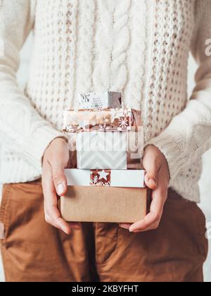 Femme en pull blanc à maille torsadée avec motif scandinave et pantalon chino marron. Pile de cadeaux de Noël entre les mains. Tenue décontractée pour New Yea Banque D'Images