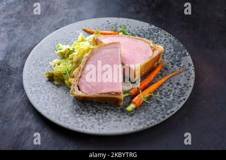 Steak de porc Kasseler en croûte de pâte avec chou de savoie et carottes servi en gros plan sur une assiette de style nordique Banque D'Images