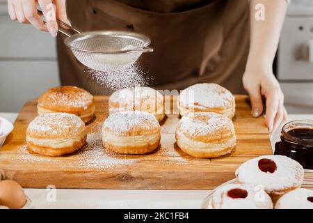 La femme prépare des beignets frais avec de la confiture dans la cuisine.Cuisine traditionnelle juive Hanoukkah sufganiyot.Saupoudrer les mains de Berliners de sucre en poudre. Banque D'Images