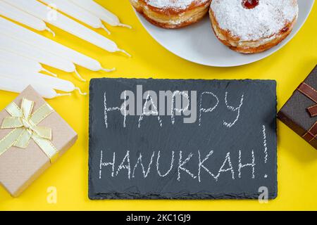 Happy Hanukkah. Jewish dessert Sufganiyot on yellow background. Symbols of religious Judaism holiday. Donuts, candles and gifts. Stock Photo