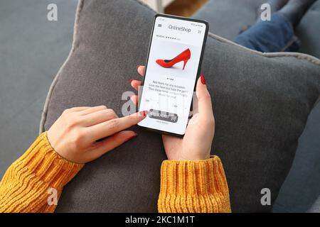 Gros plan sur une femme effectuant des achats en ligne sur un smartphone à la maison. Vue arrière de la main femme touchant l'écran tout en sélectionnant des chaussures sur le portail de commerce électronique. Banque D'Images