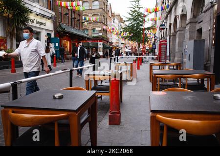 Un homme portant un masque facial passe devant des tables extérieures vides sur Gerrard Street dans Chinatown à Londres, en Angleterre, sur 16 octobre 2020. Londres doit être placée sous le « niveau 2 » mesures de verrouillage du coronavirus à partir de minuit ce soir, ce qui signifie une alerte « élevée » pour le covid-19. Plus particulièrement, ce changement va introduire une interdiction pour les personnes de différents ménages de se mélanger n'importe où à l'intérieur, ce qui suscitera une inquiétude particulière au sein de l'industrie hôtelière déjà gravement touchée. (Photo de David Cliff/NurPhoto) Banque D'Images