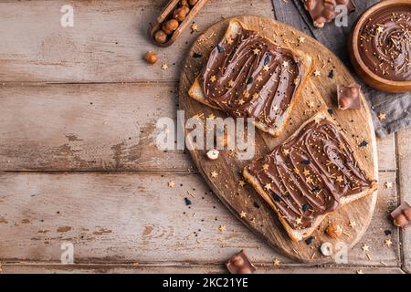 Planche de pain avec pâte de chocolat et bonbons de fête saupoudrer et noisettes sur fond de bois. Nourriture populaire de dessicer. Vue de dessus. Banque D'Images