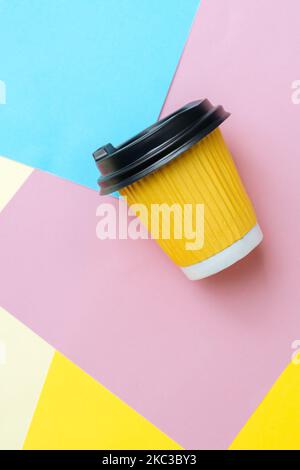 La mise au point sélective douce sur une tasse de café à emporter se trouve dans un désordre créatif sur du papier coloré sur la table de paramétrage. Fond bleu, orange et rose. Copier l'espace pour le texte. Photo verticale Banque D'Images