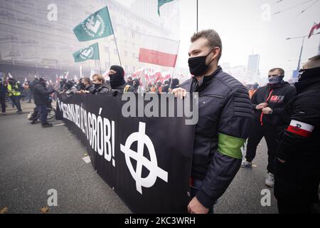 Un homme tient une bannière avec la croix celtique, un symbole de suprématie blanche à Varsovie, en Pologne, le 11 novembre 2020. Malgré l'intention des organisateurs de la Marche de l'indépendance de tenir un défilé uniquement en voiture plusieurs milliers de personnes ont pris part à pied. Onlhy minutes après le début de la marche traditionnelle les participants se sont calés avec la police anti-émeute. Les émeutiers ont lancé des bouteilles de verre, des pots de fleurs et des briques à la police anti-émeute qui a répondu par un spray au poivre. Une librairie Empik a été vandalisée après qu'une grande fenêtre de magasin a été cassée et plus tard des émeutiers ont lancé des fusées éclairantes et d'autres objets à un appartement à proximité avec un drapeau arc-en-ciel allumé Banque D'Images