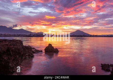 Paysage avec rochers, plages, ciel rougeâtre au crépuscule et petites îles au loin, Banque D'Images