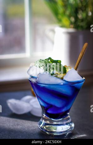 Gros plan sur un cocktail bleu lagon avec glace, menthe et citron, fond gris Banque D'Images