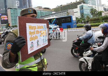 Les officiers de l'unité de police de la fonction publique du gouvernement provincial de Djakarta (Satpol PP) présentent des affiches contenant la campagne de prévention Covid-19 aux automobilistes qui traversent Jalan MH Thamrin, Menteng, Djakarta sur 30 novembre 2020. Le nombre de diffusion de Covid-19 à Jakarta n'a pas encore diminué, le gouvernement provincial DKI Jakarta continue de s'efforcer d'empêcher la propagation en rappelant aux résidents de maintenir la distance, de se laver les mains et de toujours utiliser des masques à l'extérieur. (Photo de Dasril Roszandi/NurPhoto) Banque D'Images