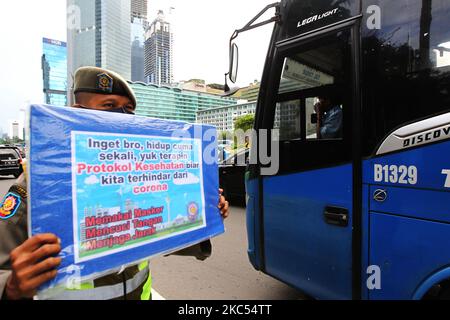 Les officiers de l'unité de police de la fonction publique du gouvernement provincial de Djakarta (Satpol PP) présentent des affiches contenant la campagne de prévention Covid-19 aux automobilistes qui traversent Jalan MH Thamrin, Menteng, Djakarta sur 30 novembre 2020. Le nombre de diffusion de Covid-19 à Jakarta n'a pas encore diminué, le gouvernement provincial DKI Jakarta continue de s'efforcer d'empêcher la propagation en rappelant aux résidents de maintenir la distance, de se laver les mains et de toujours utiliser des masques à l'extérieur. (Photo de Dasril Roszandi/NurPhoto) Banque D'Images