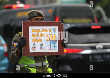 Les officiers de l'unité de police de la fonction publique du gouvernement provincial de Djakarta (Satpol PP) présentent des affiches contenant la campagne de prévention Covid-19 aux automobilistes qui traversent Jalan MH Thamrin, Menteng, Djakarta sur 30 novembre 2020. Le nombre de diffusion de Covid-19 à Jakarta n'a pas encore diminué, le gouvernement provincial DKI Jakarta continue de s'efforcer d'empêcher la propagation en rappelant aux résidents de maintenir la distance, de se laver les mains et de toujours utiliser des masques à l'extérieur. (Photo de Dasril Roszandi/NurPhoto) Banque D'Images