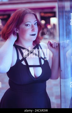 Une femme caucasienne en rouge à lèvres noir et robe noire penchée au mur et regardant la caméra Banque D'Images
