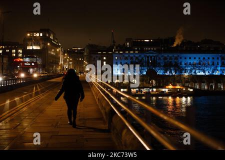 Une femme traverse le pont de Waterloo tandis que la Somerset House, éclairée en bleu en l'honneur du personnel du NHS et d'autres travailleurs de première ligne, se trouve à Londres, en Angleterre, sur 7 janvier 2021. L'Angleterre a commencé cette semaine un troisième confinement national du coronavirus, alors que les autorités s'inquiétaient que le National Health Service pourrait bientôt être submergé par des personnes souffrant de covid-19. Pendant ce temps, le Premier ministre britannique Boris Johnson a annoncé aujourd’hui que 1,5m 000 personnes à travers le Royaume-Uni ont désormais reçu au moins une première dose d’un vaccin Covid-19, avec des plans pour des centaines de milliers de vaccins à administrer chaque jour à partir du milieu de cette période Banque D'Images