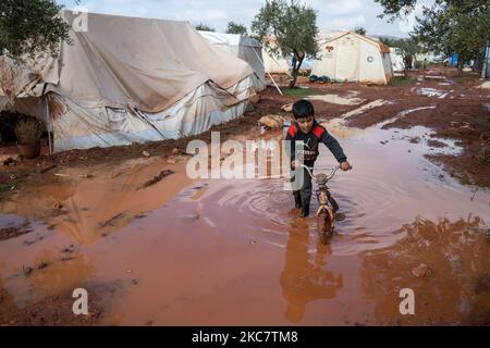 Un jeune garçon syrien tire son vélo dans l'eau boueuse du camp de réfugiés de Zaitoun après une forte tempête qui a conduit à une inondation dans les camps de réfugiés syriens d'Idlib sur 19 janvier 2021 (photo de Karam Almasri/NurPhoto) Banque D'Images