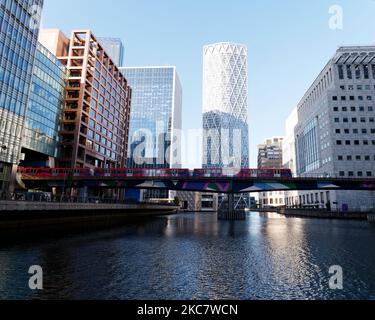 Architecture dans la région de Canary Wharf à Londres, Angleterre. Un train DLR passe sur un pont au-dessus de l'eau avec de hautes élévations derrière Banque D'Images