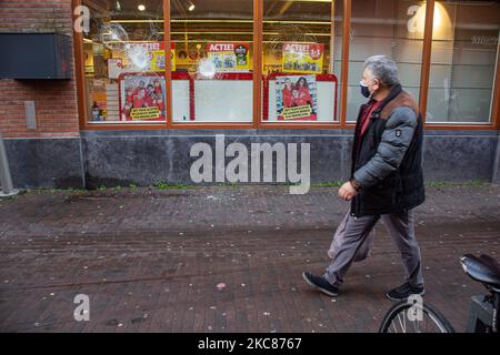 Un homme avec un masque passe devant les lunettes de façade endommagées Kruidvat. Les conséquences des troubles anti-couvre-feu à Rotterdam. Fenêtres endommagées de magasins, cafés, chaîne de restauration rapide, chaussée détruite, distributeurs de billets cassés, Les arrêts de bus, les arrêts de tramway, les fenêtres et les lunettes endommagées même dans un quartier résidentiel ont été causés par les violents manifestants qui se sont affrontés avec la police et ont pillé le quartier autour de Groene Hilledijk, Beijerlandselaan et Randweg. C'est la nuit consécutive de 3rd émeutes et affrontements avec les politiques après que le gouvernement a imposé le couvre-feu pour lutter contre la propagation du Covid-19 Coronav Banque D'Images