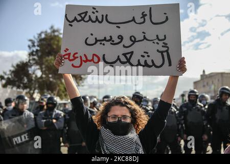 Une jeune manifestante féminine pose un écriteau qui se lit en arabe : « il y a un véhicule blindé entre la représentante du peuple et le peuple » alors qu’elle se tient devant les membres des forces de sécurité formant un mur pour empêcher ses camarades (non illustré) De manifester devant le bâtiment de l'Assemblée des représentants du peuple (ARP) (Parlement tunisien) à Bardo. Des dizaines de jeunes du quartier difficile de Hay Ettadhamen, l'une des villes les plus peuplées de Tunis, sont descendus dans la rue dans une marche de protestation anti-gouvernementale qui a commencé à partir de leur voisinage Banque D'Images