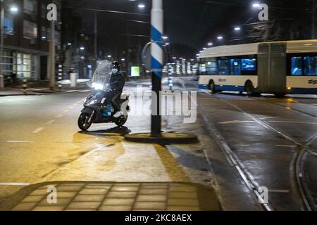 Une moto-scooter avec le conducteur portant un masque facial et un bus vide dans les rues. Rues vides et calmes de la ville néerlandaise d'Amsterdam pendant le couvre-feu COVID. Les gens ne peuvent être dehors qu'avec une raison prouvée et une autorisation spéciale avec la documentation appropriée sinon ils sont condamnés à une amende de 95euro, à l'heure du couvre-feu de nuit. Les transports en commun comme le bus et le tram passent vides. Des policiers et des véhicules ont été déployés à Amsterdam pour donner un aperçu du couvre-feu. Les rues désertes du sont vues au quatrième jour avec le couvre-feu dans le pays, plus calmes après de violentes manifestations et des affrontements les jours précédents. C Banque D'Images