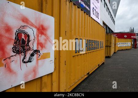 Un signe d'un homme avec un masque de protection chimique vu vandalisé avec des graffitis sur les contenants. Le stade du club PSV de Philips Stadion, situé dans la ville néerlandaise d'Eindhoven, est barricadé de conteneurs d'expédition pour protéger le bâtiment, le musée, le magasin d'air, les portes multiples, le côté piste et les supporters contre les émeutes et le pillage comme cela s'est produit précédemment dans la ville. La fortification et le scellement de l'avant du stade ont eu lieu après que le club a reçu quelques menaces selon les médias locaux. Eindhoven a été confronté à des affrontements violents lors d'une manifestation anti-blocage/anti-couvre-feu qui m'a tourné Banque D'Images