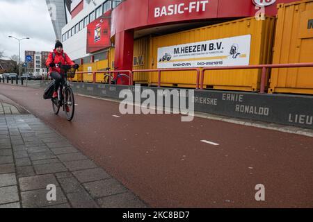 Personnes passant devant les conteneurs d'expédition à l'extérieur du stade, vélo sur des vélos. Le stade du club PSV de Philips Stadion, situé dans la ville néerlandaise d'Eindhoven, est barricadé de conteneurs d'expédition pour protéger le bâtiment, le musée, le magasin d'air, les portes multiples, le côté piste et les supporters contre les émeutes et le pillage comme cela s'est produit précédemment dans la ville. La fortification et le scellement de l'avant du stade ont eu lieu après que le club a reçu quelques menaces selon les médias locaux. Eindhoven a été confronté à des affrontements violents lors d'une manifestation anti-blocage/anti-couvre-feu qui s'est transformée en Banque D'Images